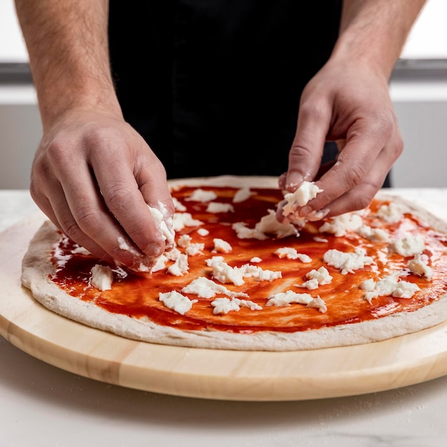 Free photo man putting mozzarella on pizza dough