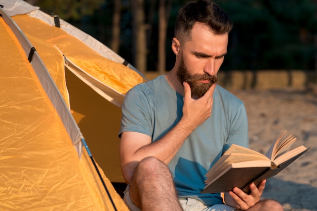 Free photo man reading a book next to tent