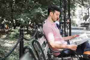 Free photo man reading newspaper on bench