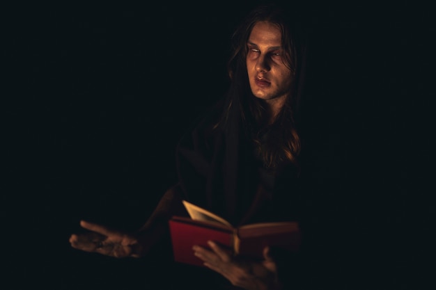 Man reading a red spell book in the dark and looking away