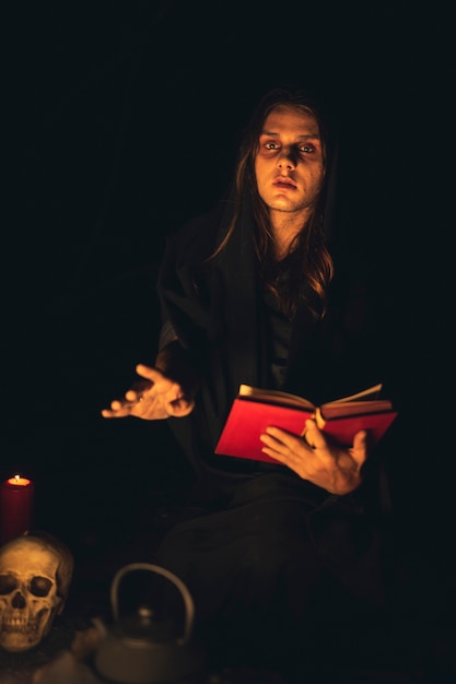 Free Photo man reading a red spell book in the dark and looking at camera