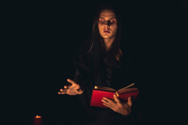 Free photo man reciting a red spell book in the dark