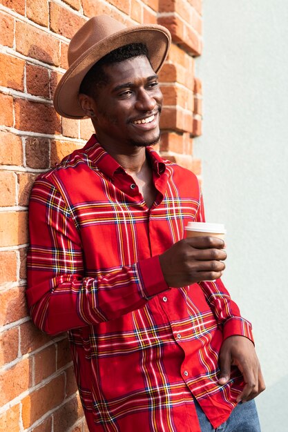 Man in red shirt leaning on a wall and holding a coffee