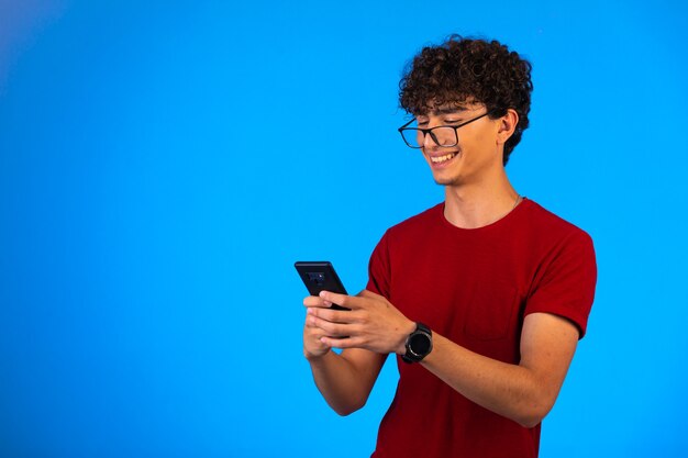 Man in red shirt taking selfie on a smartphone on blue and laughing.