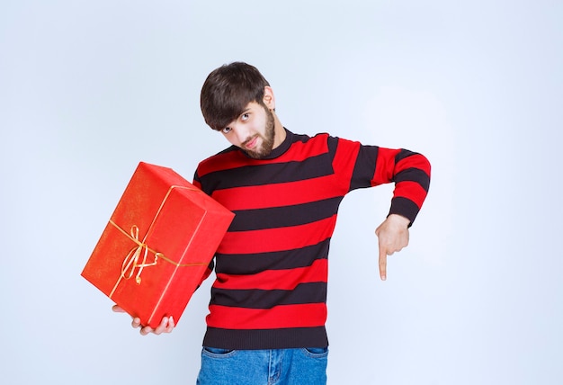 Free photo man in red striped shirt holding a red gift box and calling the person right next to him.