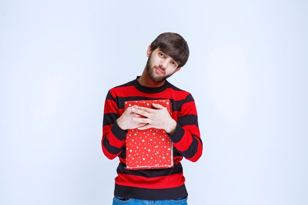 Man in red striped shirt holding a red gift box and hugging it tight and do not want to share with anybody.