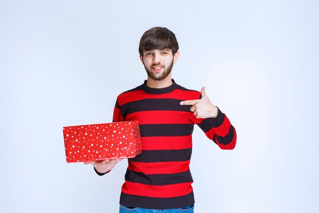 Man in red striped shirt with a red gift box and calling someone to present it.