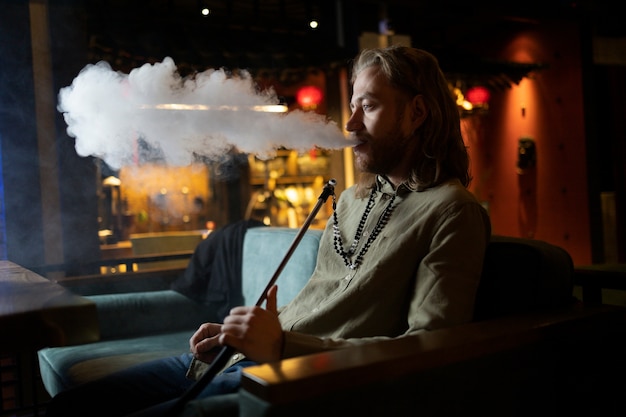 Free Photo man relaxing by vaping from a hookah in a bar