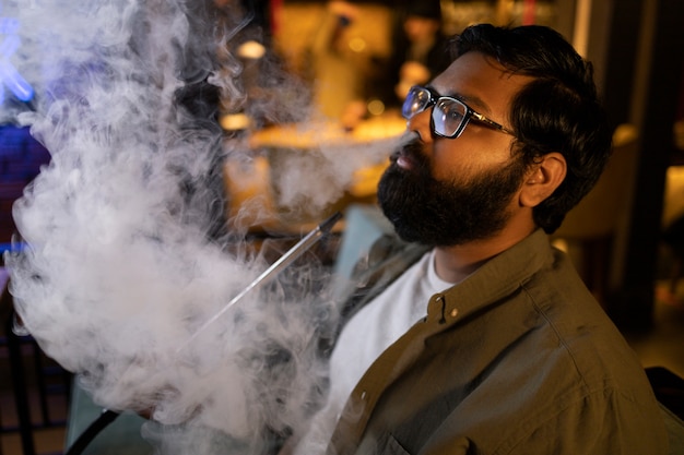 Man relaxing by vaping from a hookah in a bar