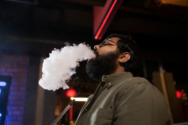 Free photo man relaxing by vaping from a hookah in a bar