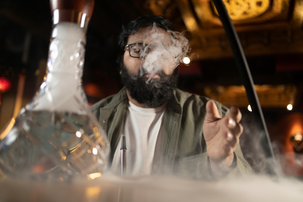 Free photo man relaxing by vaping from a hookah in a bar