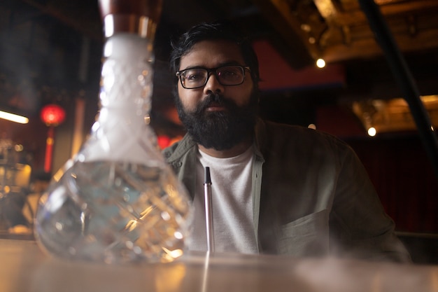 Free photo man relaxing by vaping from a hookah in a bar