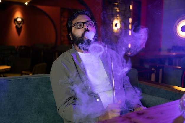 Free photo man relaxing by vaping from a hookah in a bar