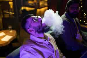 Free photo man relaxing by vaping from a hookah in a bar