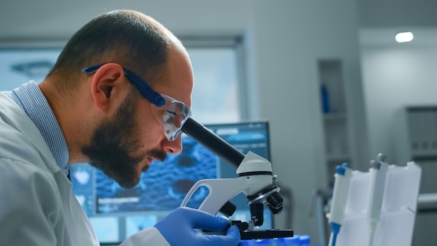 Free photo man research scientist looking at samples under microscope in modern equipped laboratory