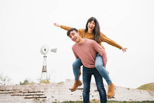 Man riding laughing woman piggyback having fun in nature