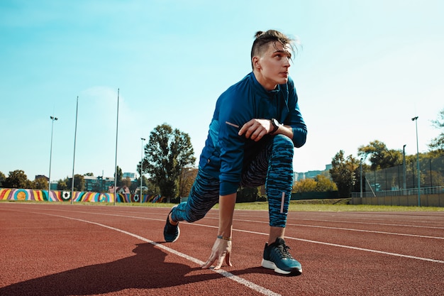 Man runner stretching legs preparing for run training on stadium tracks doing warm-up