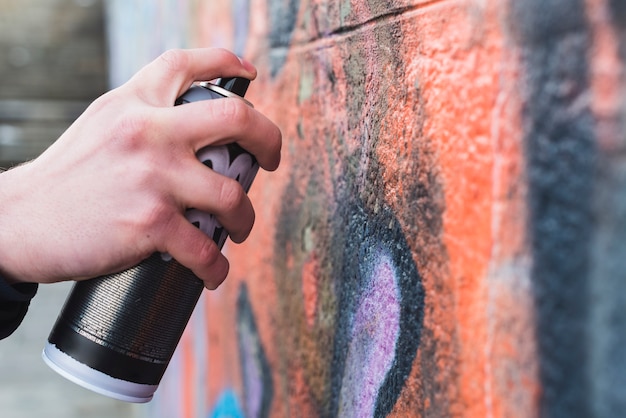 Free photo man's hand drawing graffiti on wall with aerosol can