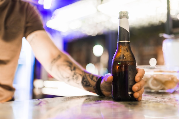 Free Photo man's hand holding alcohol bottle on bar counter