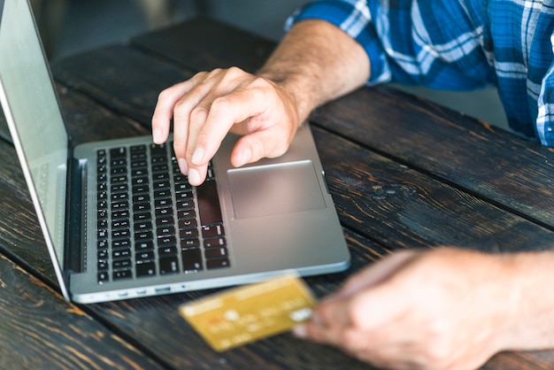 Free Photo man's hand holding credit card typing on laptop over the wooden desk