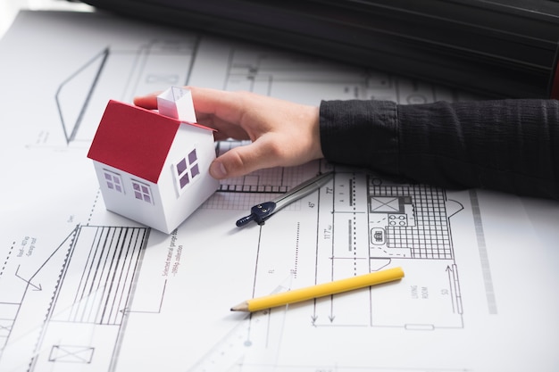 Man's hand holding house model on blueprint at office