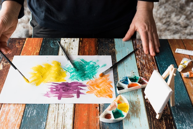 Free photo man's hand painting colorful brushstroke on white paper