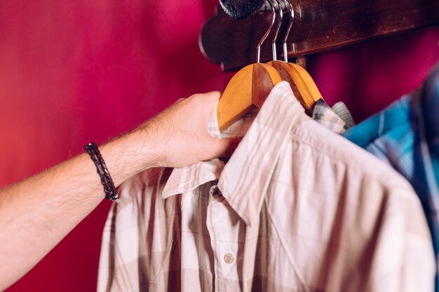 Man's hand taking coat hanger shirt from the rack hook on red wall