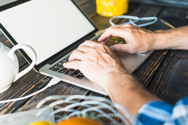 Man's hand typing on laptop over the wooden desk