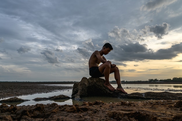 A man sat bent his knees on the base of the tree where the floor was dry and hands placed on the head.