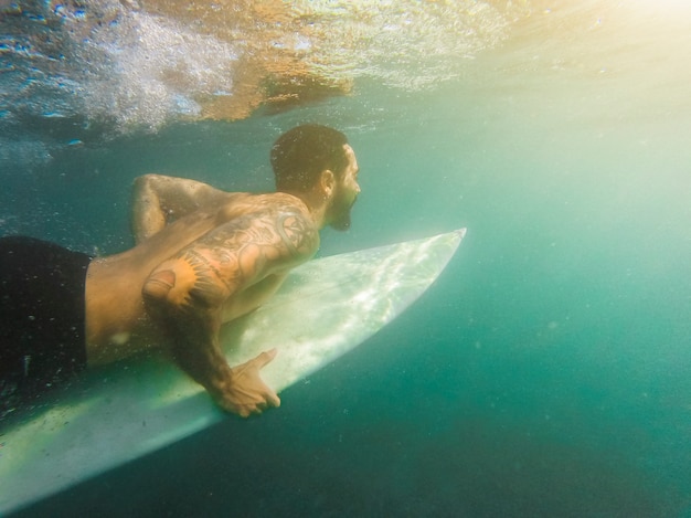 Free photo man in shorts diving with surfboard underwater