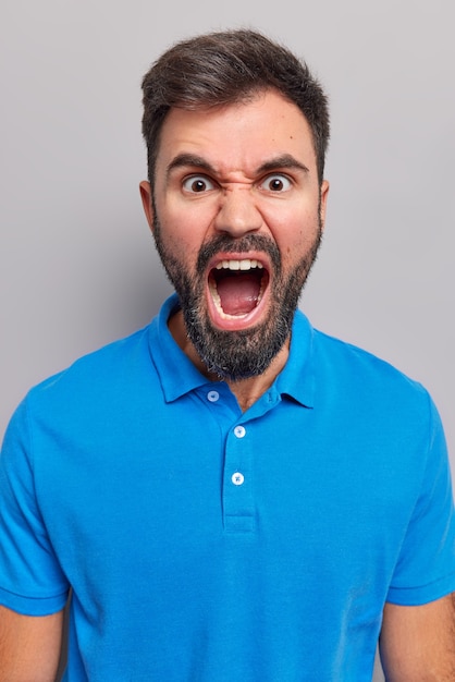 Free photo man shouts angrily keeps mouth widely opened expresses negative emotions screams furious wears casual blue t shirt isolated on grey