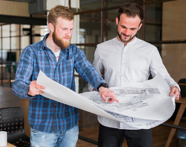 Free photo man showing blue print to his colleague at office