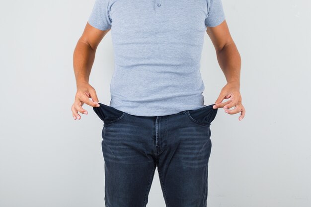 Man showing empty pockets in grey t-shirt, jeans