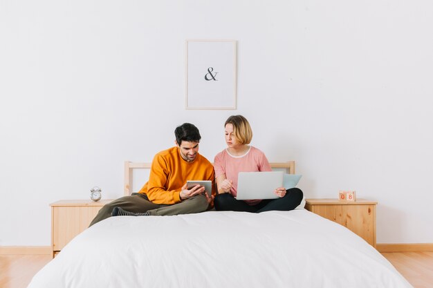 Man showing woman tablet on bed