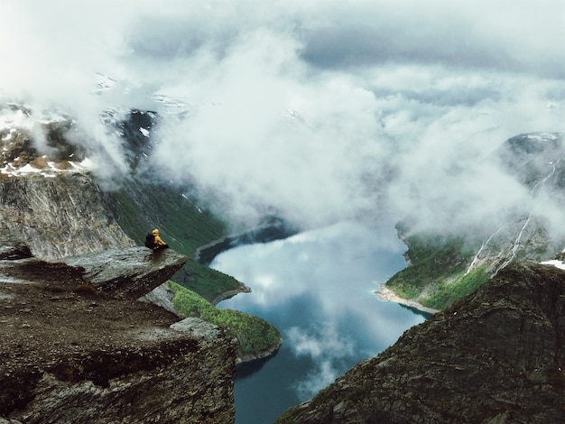 Man sits at the end of Trolltunga before the mountains