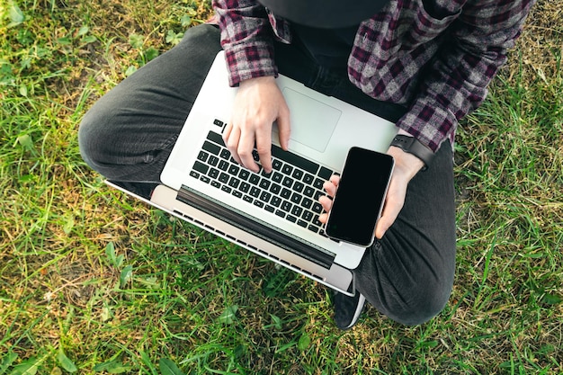 Free Photo a man sits on the grass with a laptop and smartphone top view