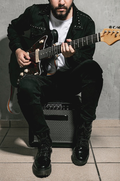 Free photo man sitting on amplifier and playing guitar