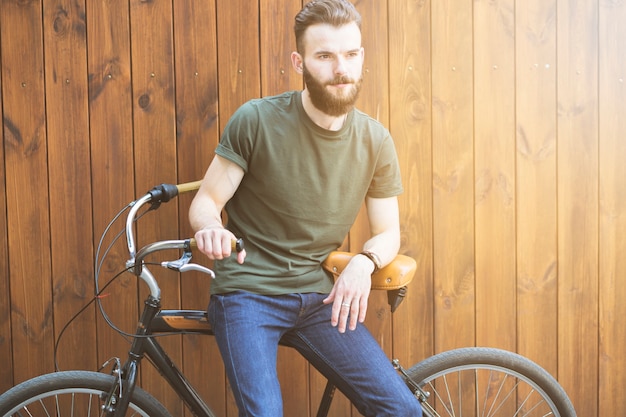 Free photo man sitting on bicycle against wooden backdrop