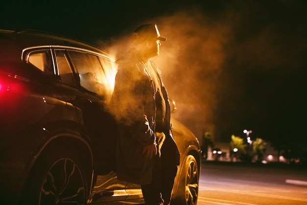 Man sitting next to car at night