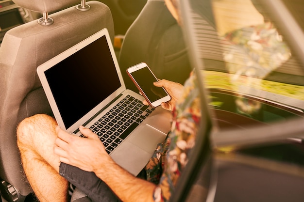 Man sitting in car with laptop and smartphone