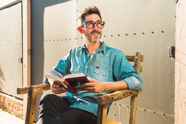 Man sitting on chair holding book in hand looking away