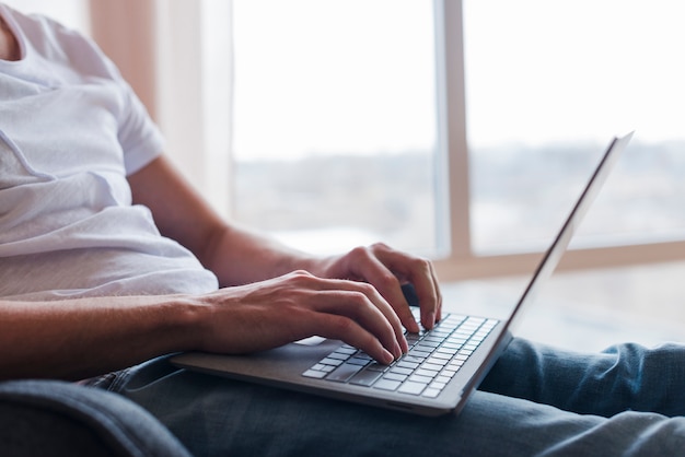 Free Photo man sitting on chair and typing on laptop near window