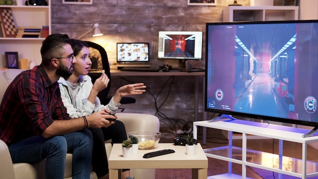 Free photo man sitting on couch playing video games on television with girlfriend next to him.