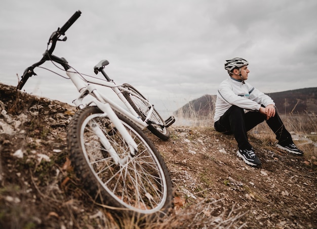 Free photo man sitting on the grass next to his mountain bike