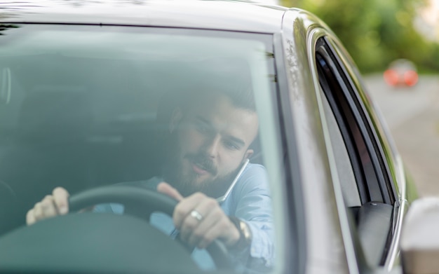 Free photo man sitting inside car talking on mobile phone seen through windscreen