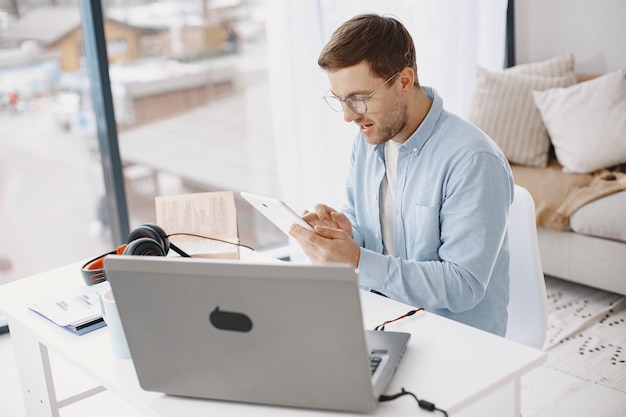 Man sitting in living room at home. Guy enjoying studying using laptop and headset. Man use a tablet.