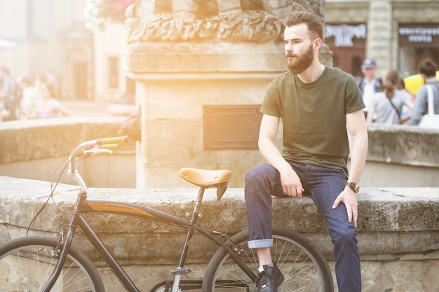 Free photo man sitting near his bicycle in city