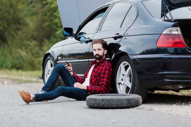 Man sitting on road and leaning on car