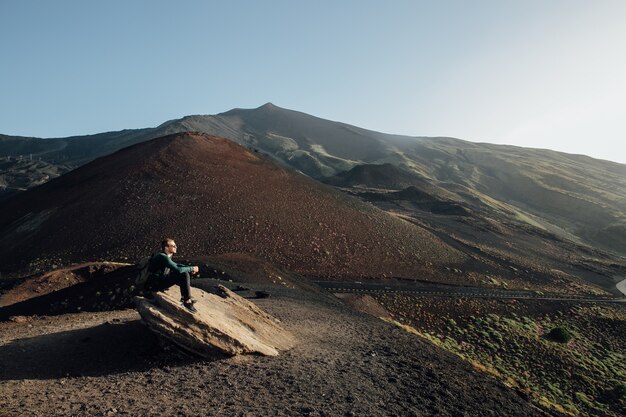 Man sitting on rock and enjoying beautiful landscape of volcano Etna in Sicily