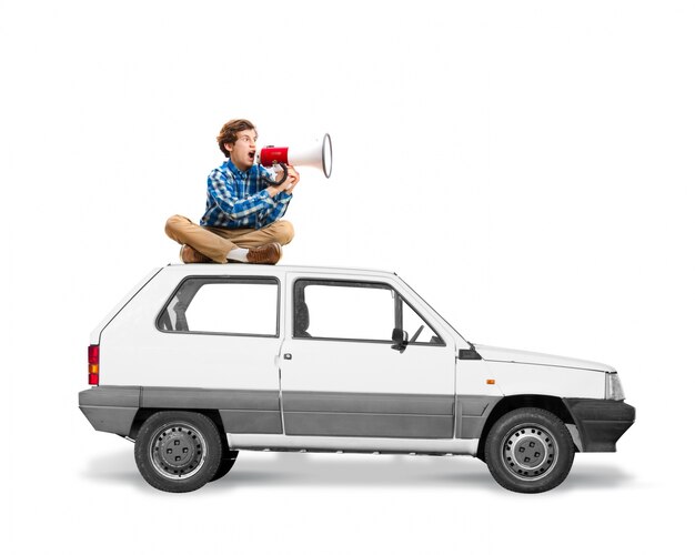 Man sitting on the roof of a car with a megaphone screaming